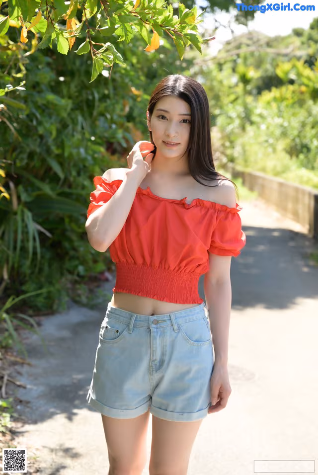 A woman in a red top and denim shorts posing for a picture.