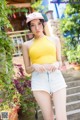 A woman in a yellow top and denim shorts posing for a picture.