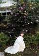 A woman in a white dress sitting in front of a bush of flowers.