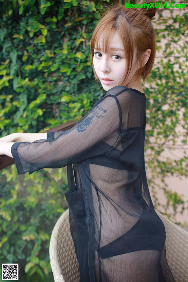 A woman in a sheer black dress posing for a picture.