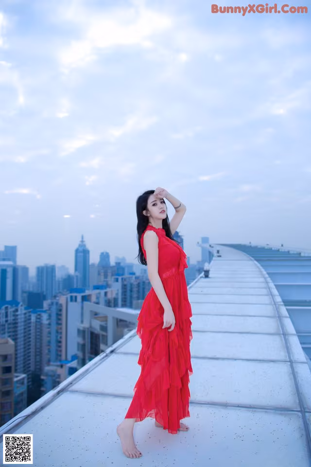 A woman in a red dress standing on top of a building.