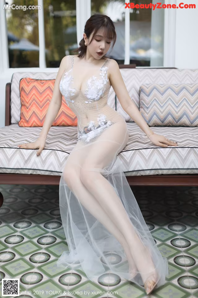 A woman in a sheer white dress sitting on a couch.
