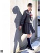 A woman in a school uniform leaning against a wall.