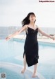 A woman in a black dress standing by a swimming pool.