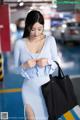 A woman in a blue dress holding a black bag.