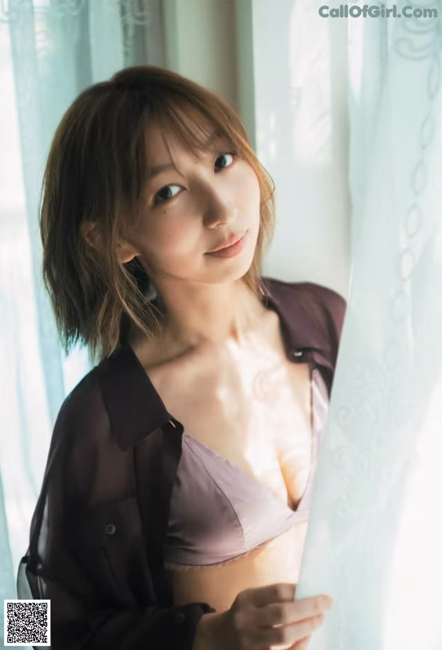 A woman in a purple shirt is posing by a window.