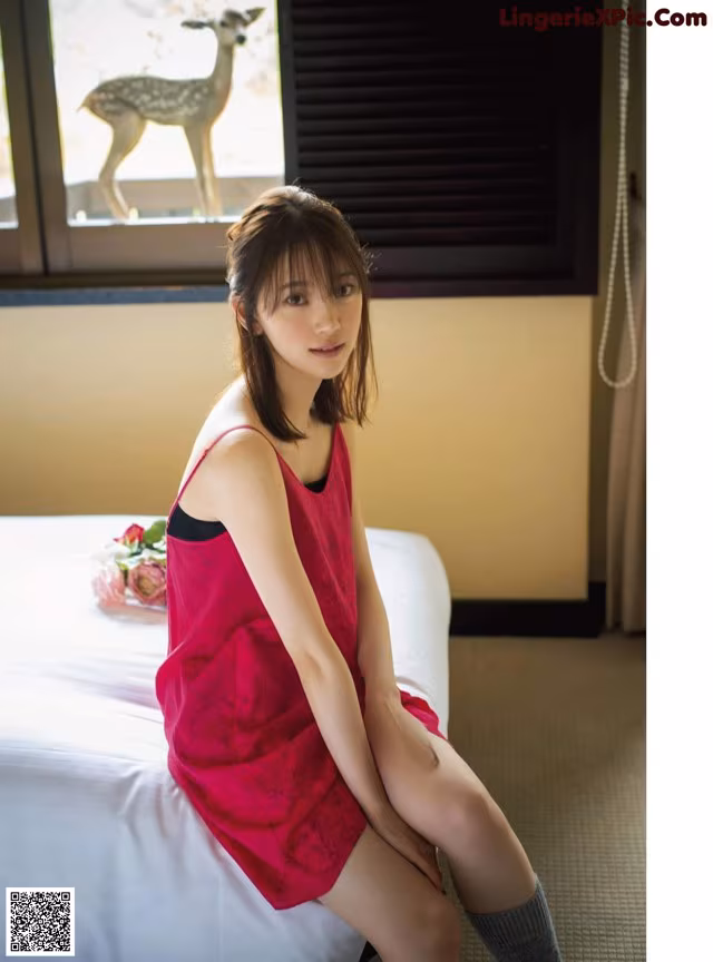 A woman in a red dress sitting on a bed.
