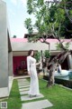 A woman in a white dress standing next to a tree.